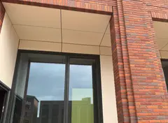 Fragment van een gevel met rode baksteen en lichte plafondpanelen.