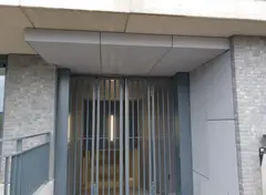 Ingang met metalen poort en bekleding van grijze platen.