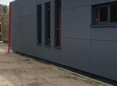 Laag gebouw met donkere grijze gevel van grote panelen.