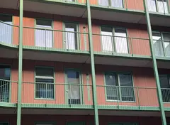 Gevel van een modern woongebouw met oranje gevelbekleding en groene balkons, raam- en deurkozijnen.