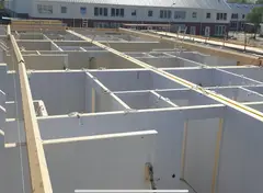 Bouwconstructie in montagefase met witte prefabwanden en houten draagbalken.