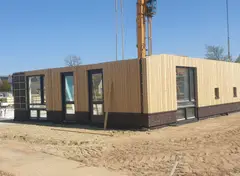 Huis in aanbouw met gevel van verticale houten latten en grote ramen.