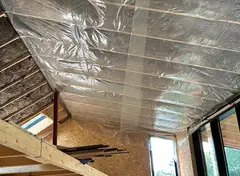 Interieur van een houten huis in aanbouw met zichtbare isolatie en dampremmende folie aan het plafond.