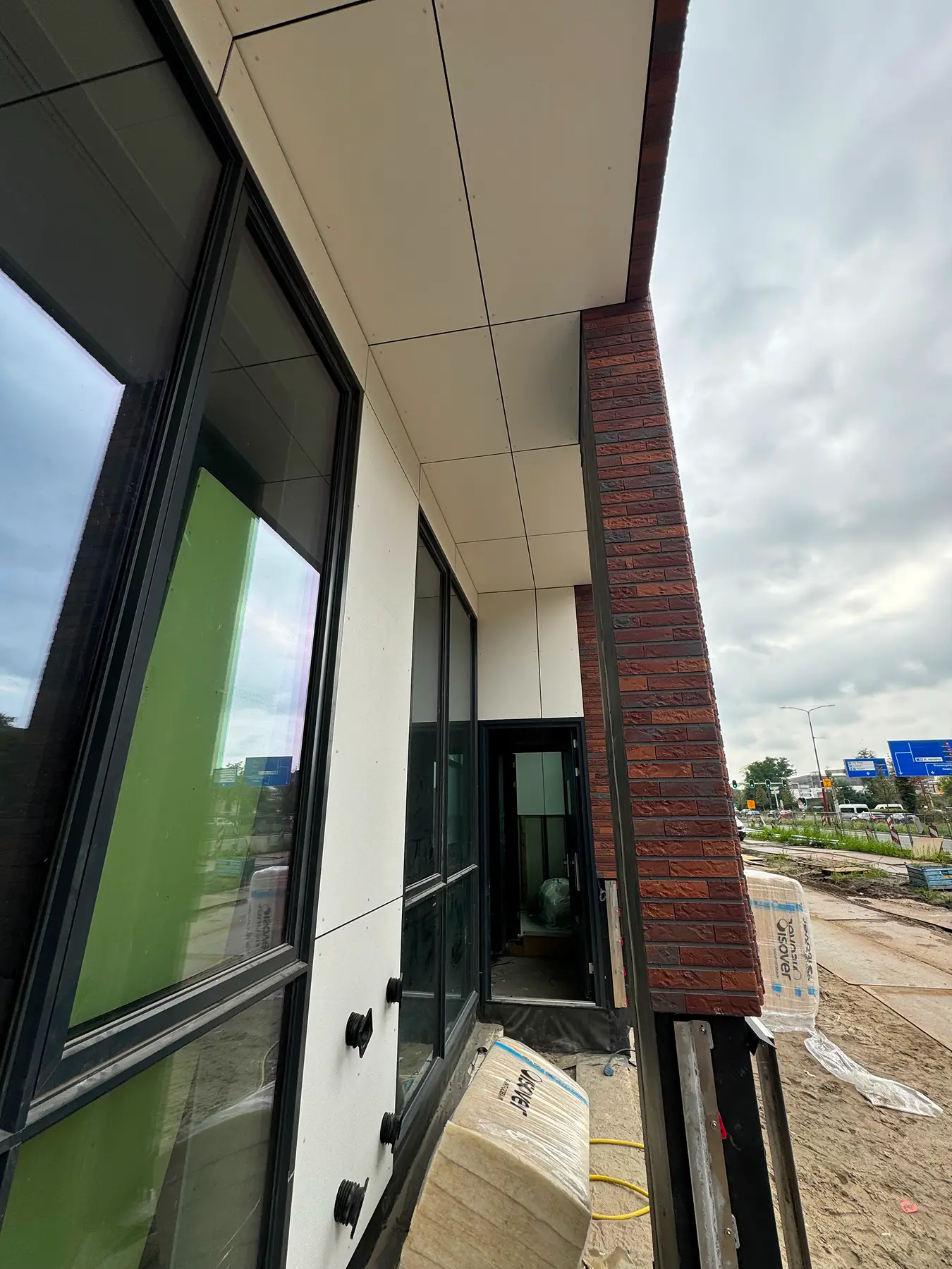 Gevel met grote ramen en lichte panelen onder de overkapping.