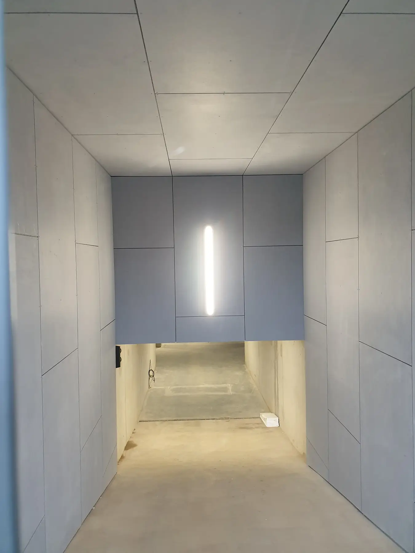 Ingang van een modern gebouw met een gebogen plafond van gevelplaten en een groene deur- en raamomlijsting.