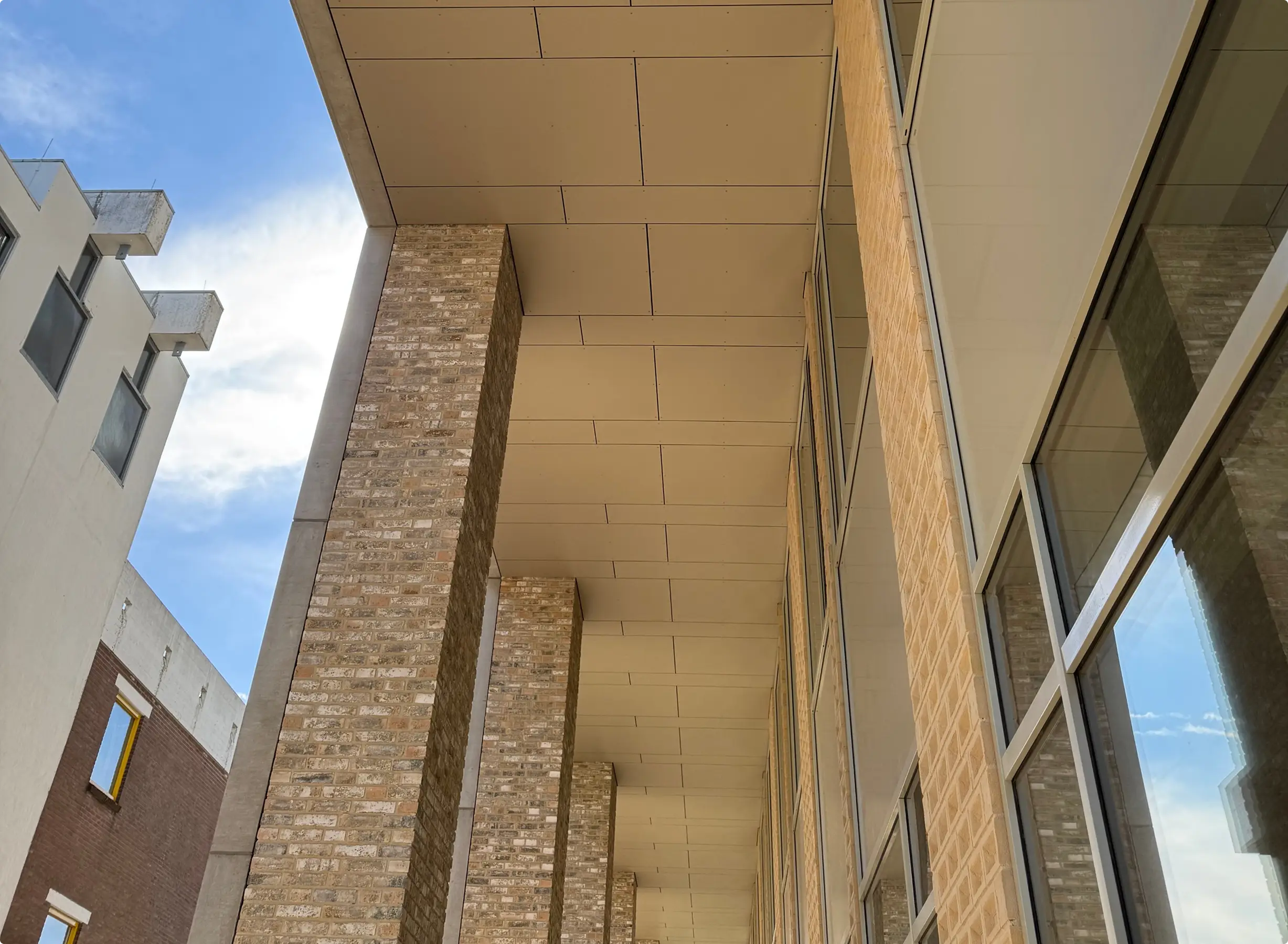 Kolonnade van lichte baksteen en plafond van gevelpanelen bij een modern gebouw.