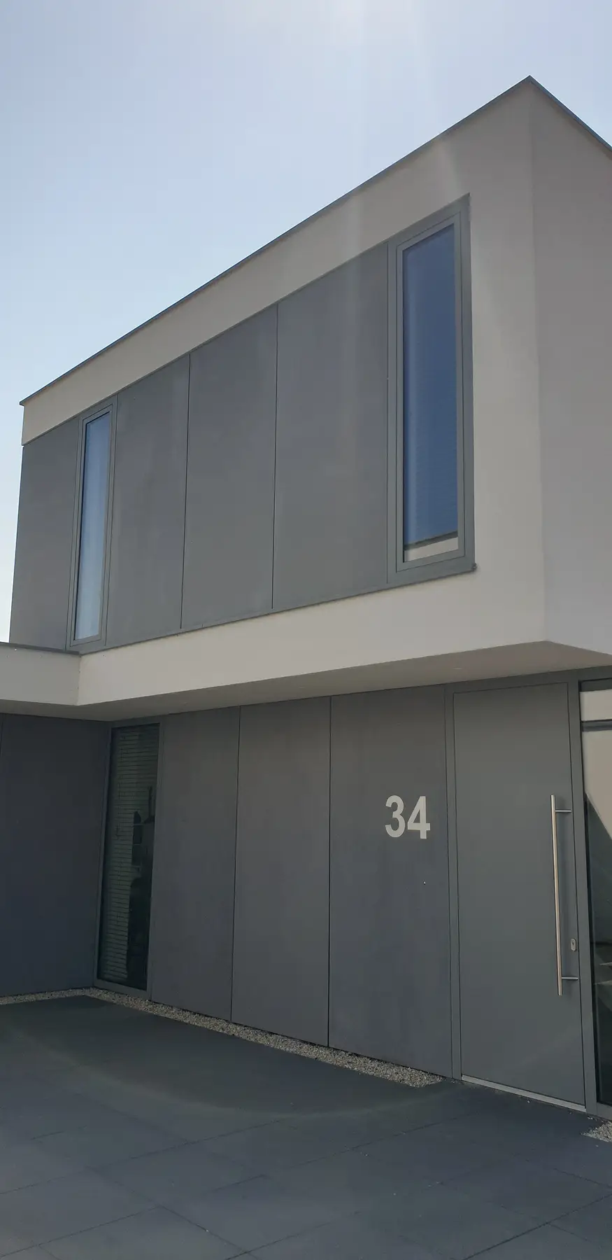 Huis met gladde grijze gevel en nummer 34 op de muur.