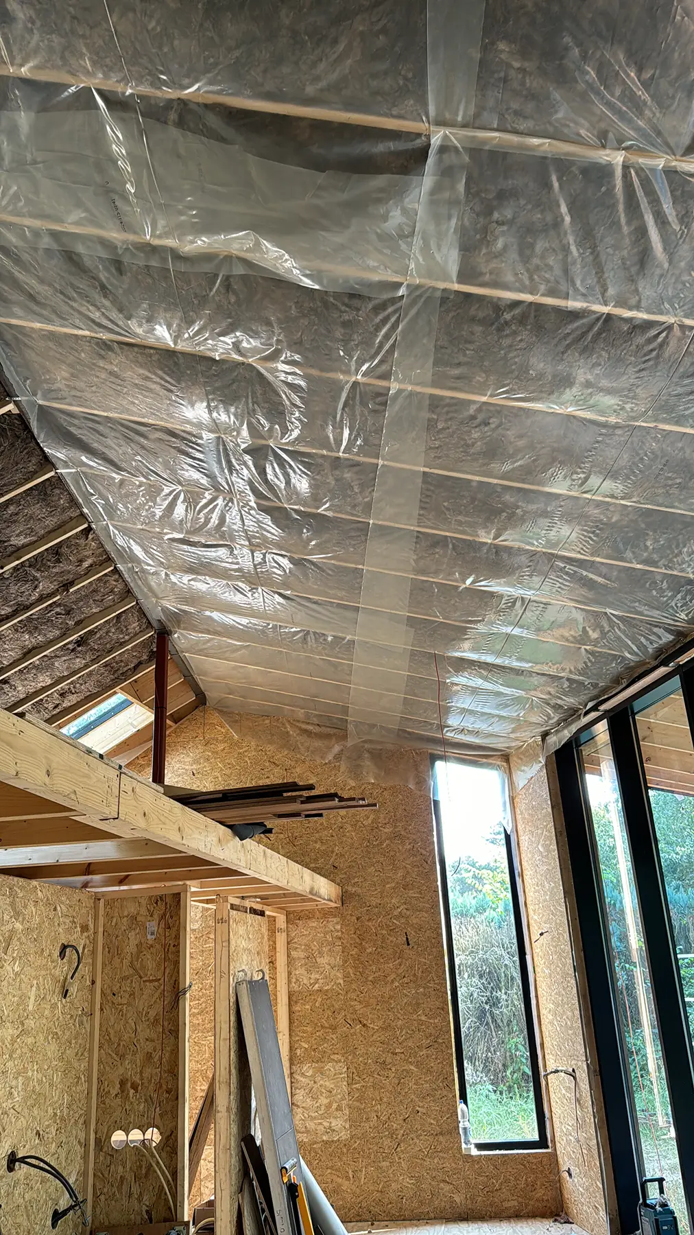 Interieur van een houten huis in aanbouw met zichtbare isolatie en dampremmende folie aan het plafond.