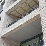 Gevel van lichte baksteen met metalen balustrade en afgewerkt balkon.
